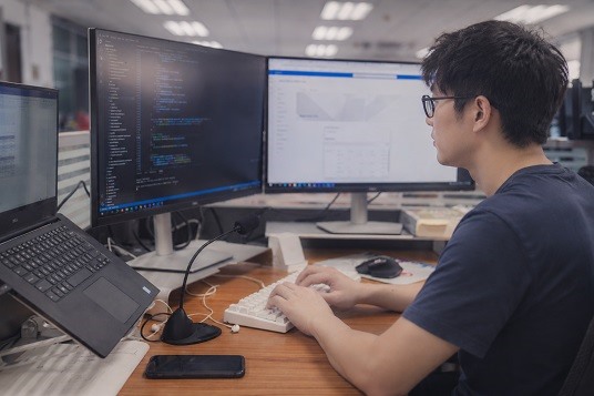 An engineer working on code at a multi-monitor desk